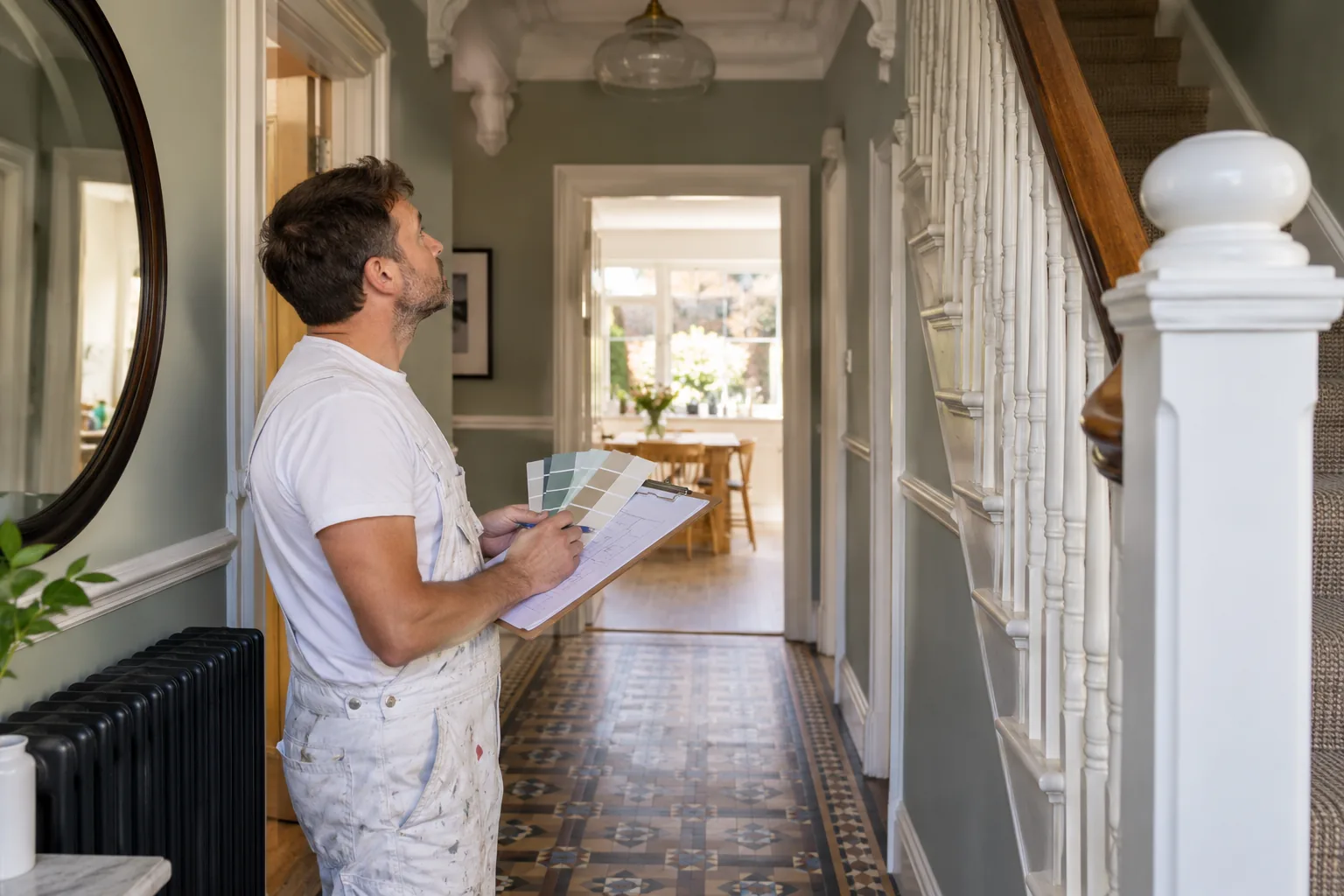 Decorator holding a colour chart and notes while surveying a hallway and staircase